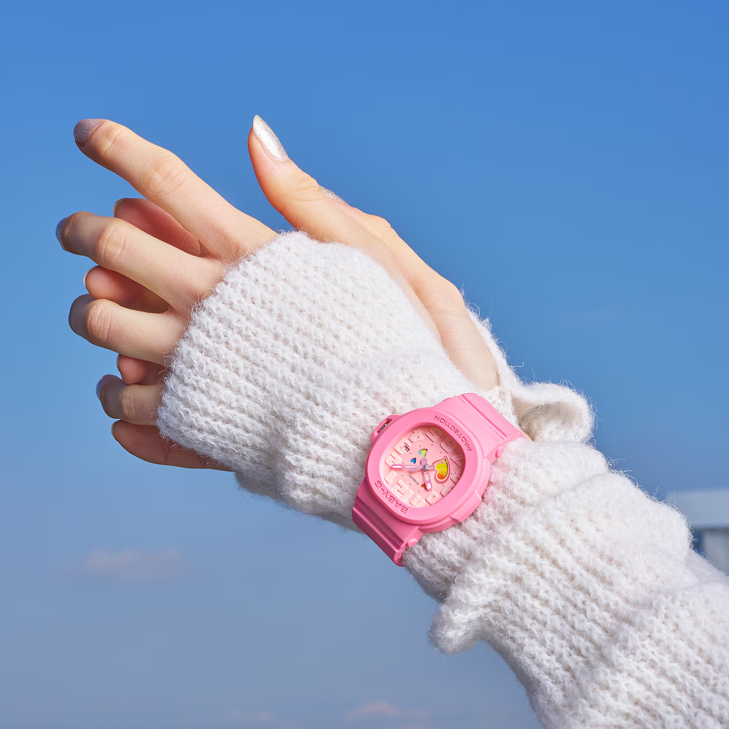 Hand wearing a white knitted glove with a pink watch against a blue sky.