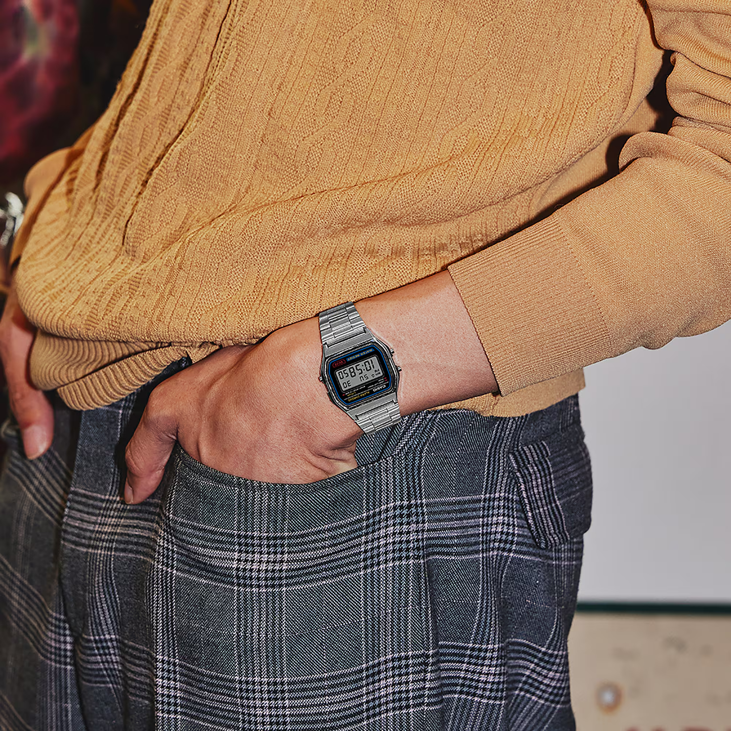Person wearing a mustard yellow sweater and plaid pants with a digital watch on their wrist.