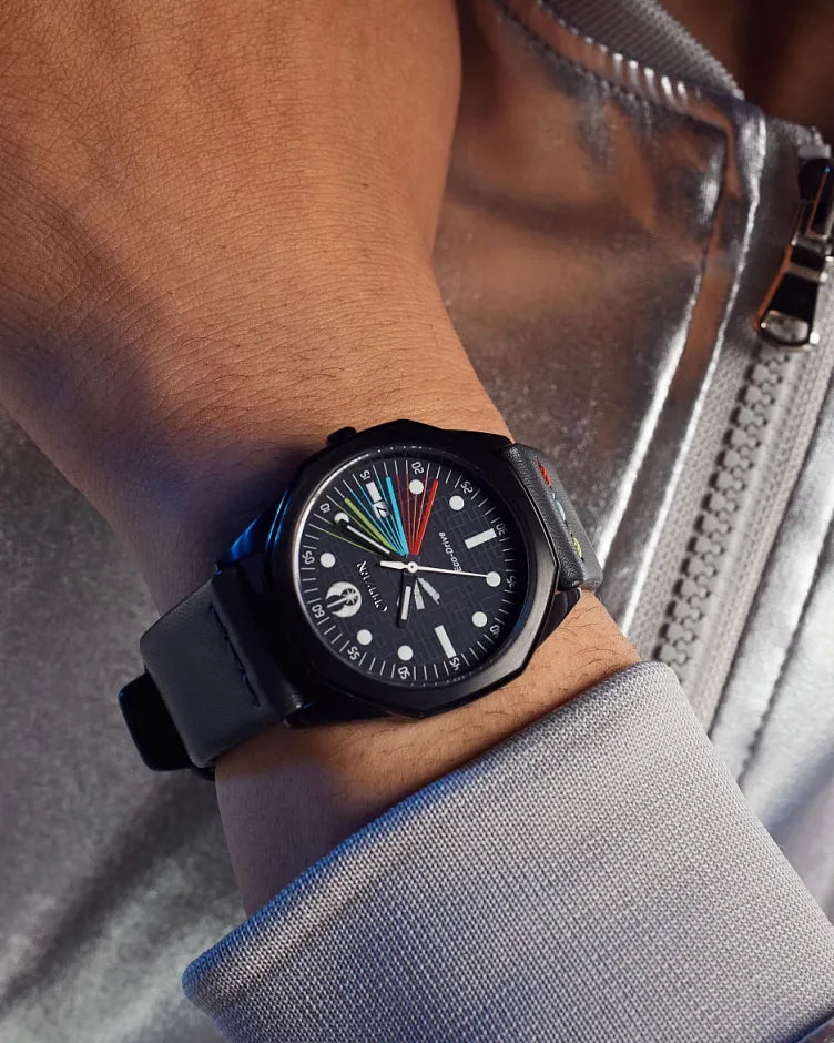 Close-up of a wrist wearing a black watch with a colorful face, against a neutral background.