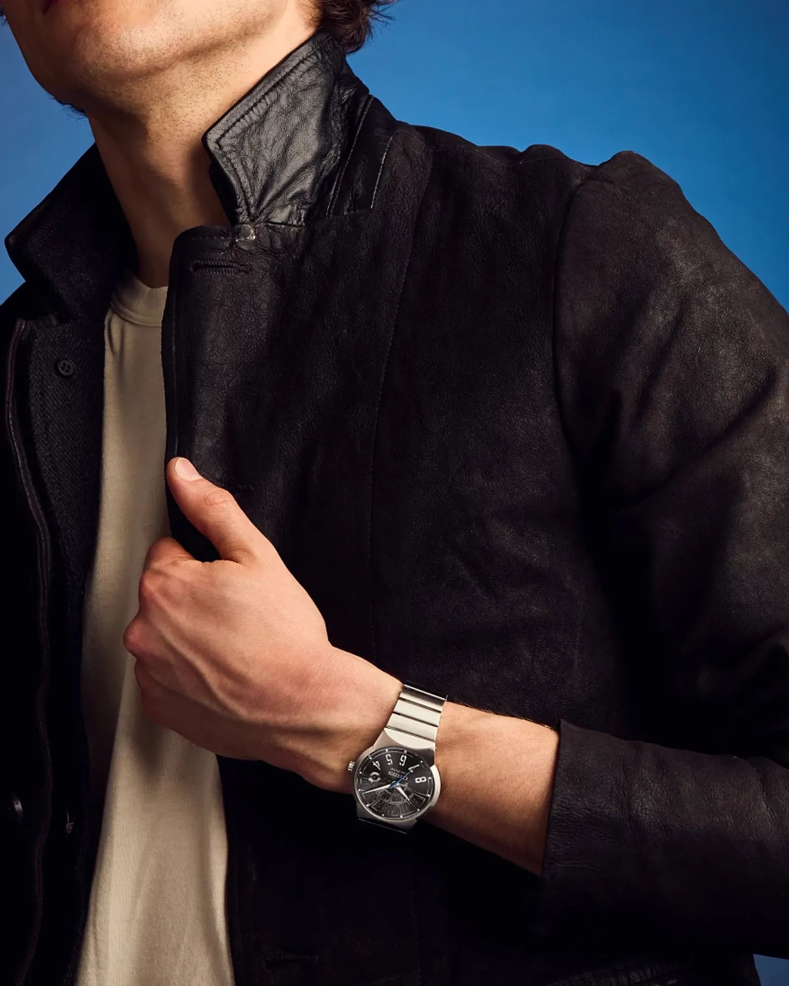 Person wearing a dark jacket and a watch on a blue background