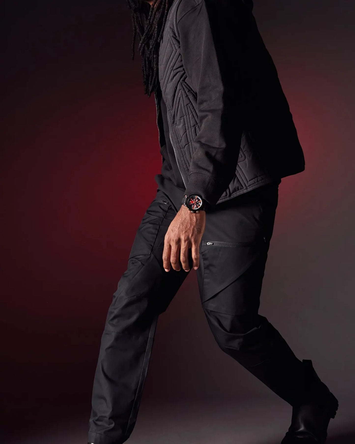 Person wearing a dark jacket and pants with a watch on a gradient background