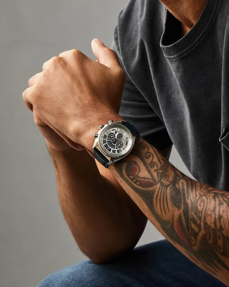 Person wearing a watch with a tattooed arm on a gray background