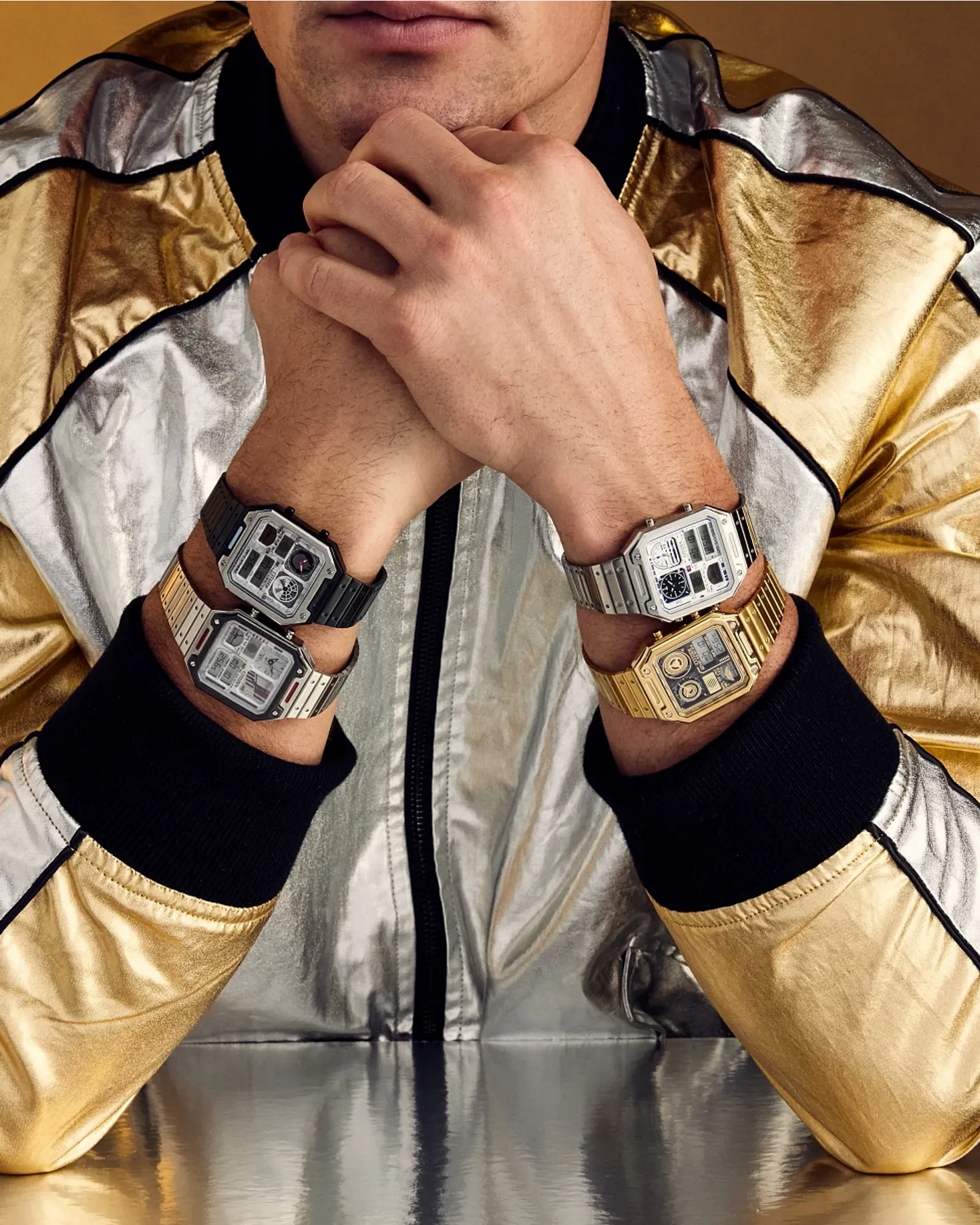 Person wearing multiple watches on each wrist with a gold and silver jacket.