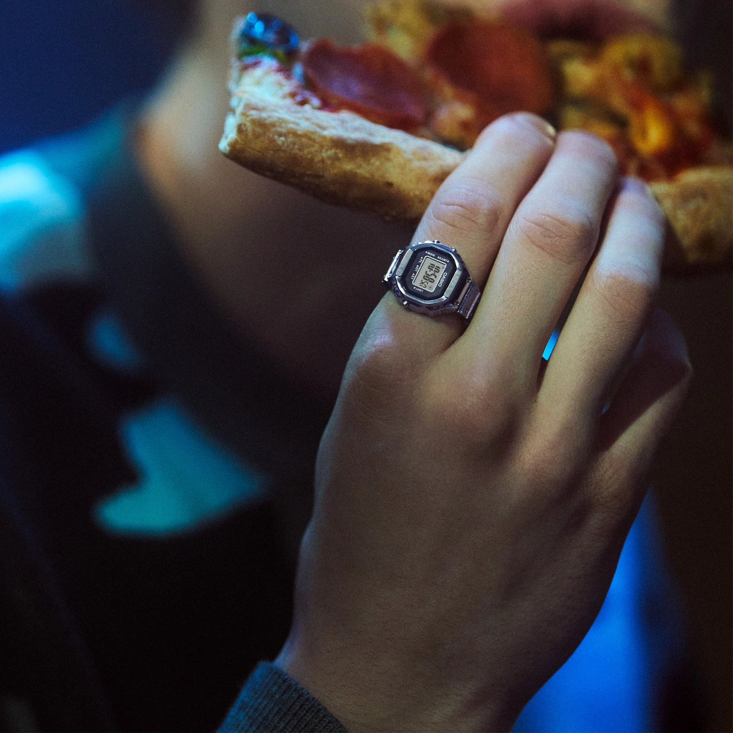 Hand holding a slice of pizza with a ring on a dark background