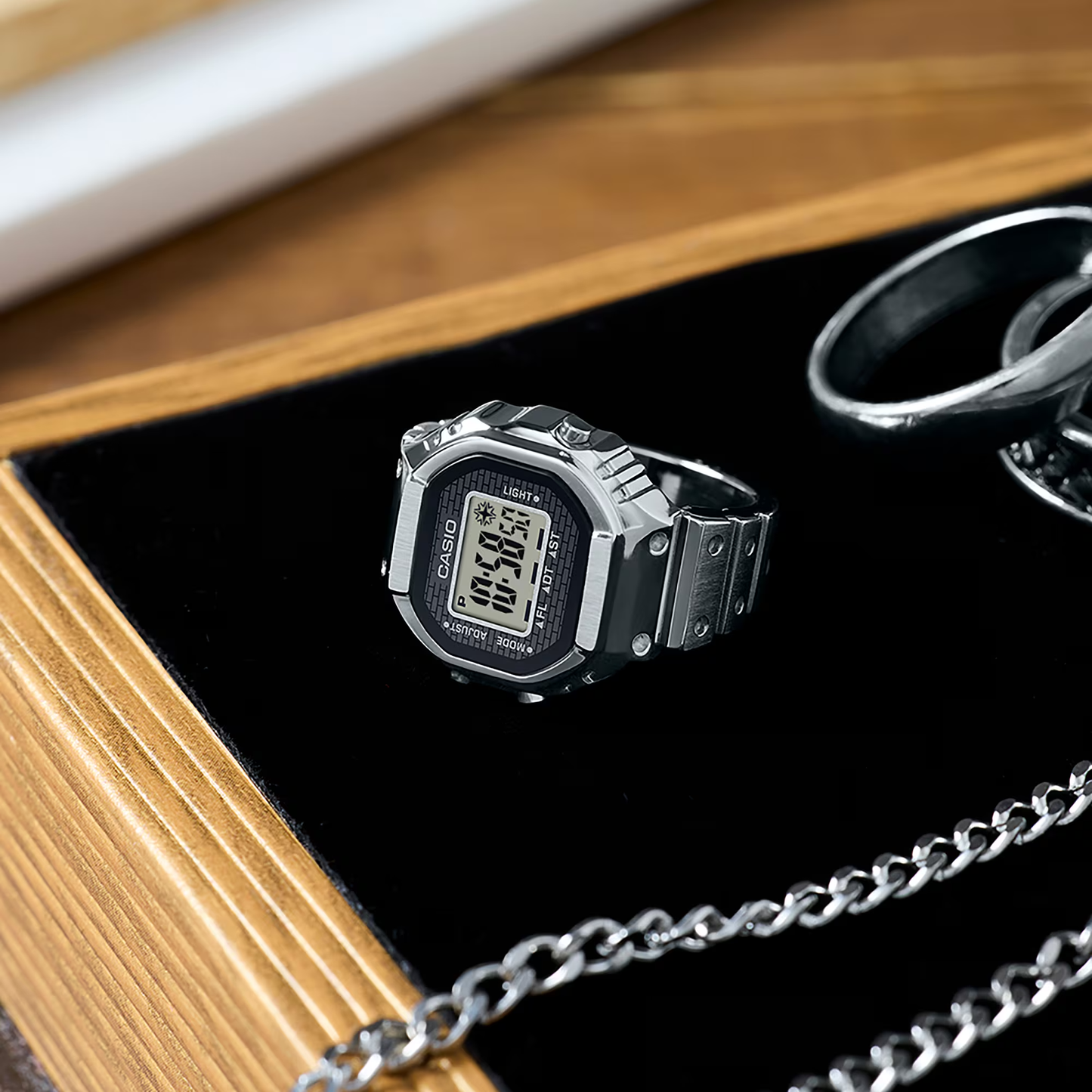 Digital watch and keychain set on a black tray with wooden surface