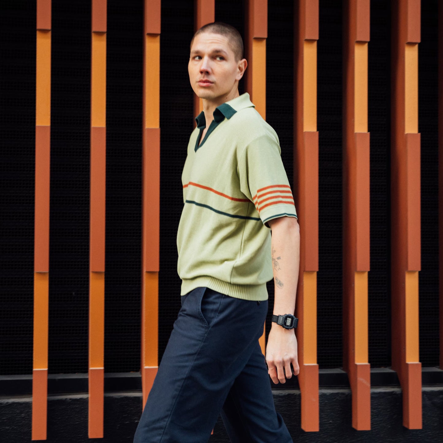 Man wearing a light green sweater with striped sleeves against a striped wall.