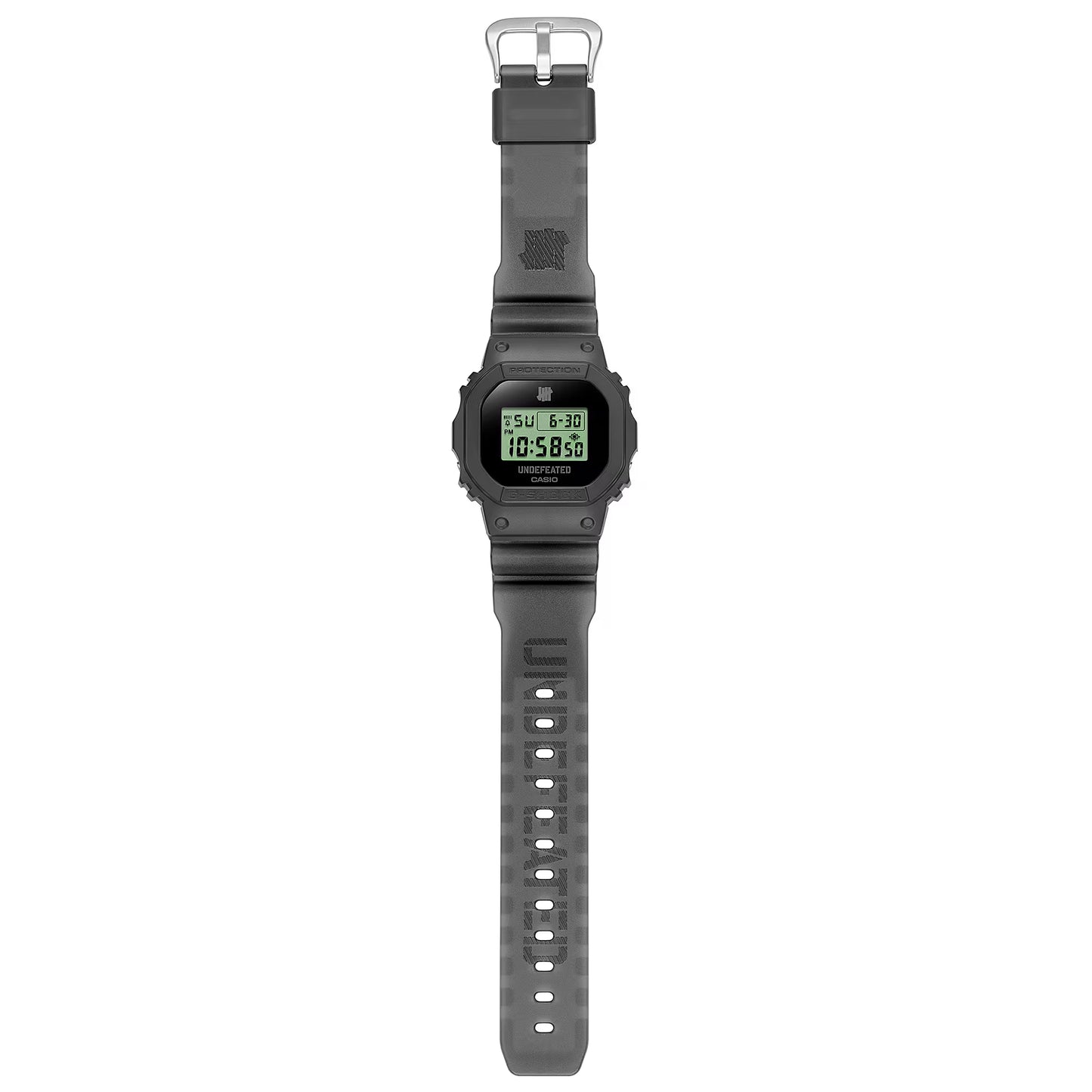 Casio G-SHOCK DWE5600UD-1 UNDEFEATED collaboration model with matte black Carbon Core Guard case, semi-translucent resin band featuring UNDEFEATED logo, green LCD display, engraved caseback, and special packaging. Includes two interchangeable camouflage straps (tiger camo, storm camo). Features shock resistance, mineral glass, 200m water resistance, LED Super Illuminator backlight, stopwatch, countdown timer, alarms, flash alert, auto-calendar, and ±15 sec/month accuracy. Case size 48.9 × 43.8 × 13.7 mm, we