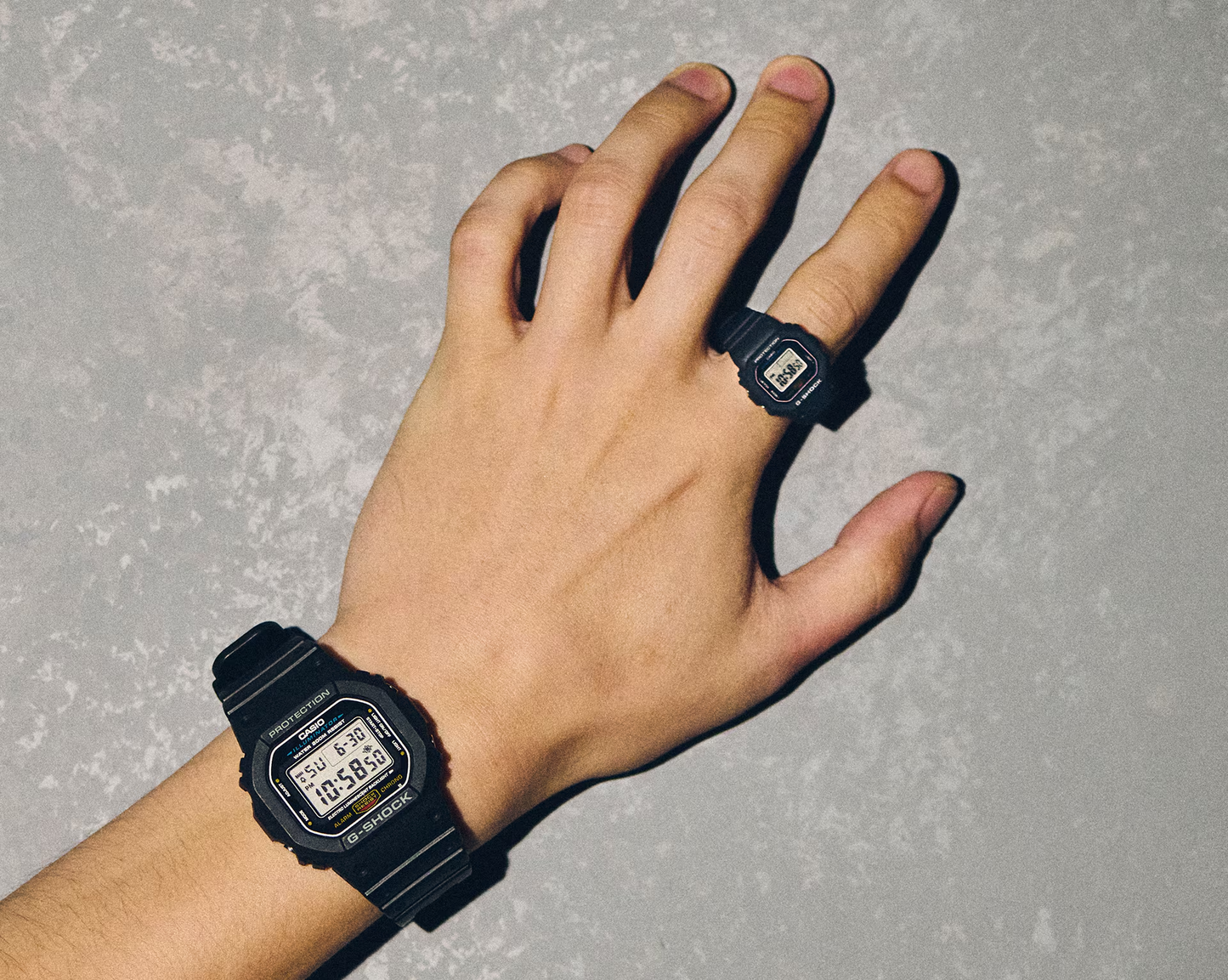 Casio G-SHOCK Nano DWN5600-4 miniature watch. 1/10-scale red version of the DW-5600 made from sustainable bio-based resin. Features 23.4 × 20 × 7.5 mm case, 6 g weight, LED backlight with time flash, dual time, stopwatch, and auto-calendar. Shock resistant and 200-meter water resistant. Includes special silicone display stand and approx. 2-year SR621SW battery