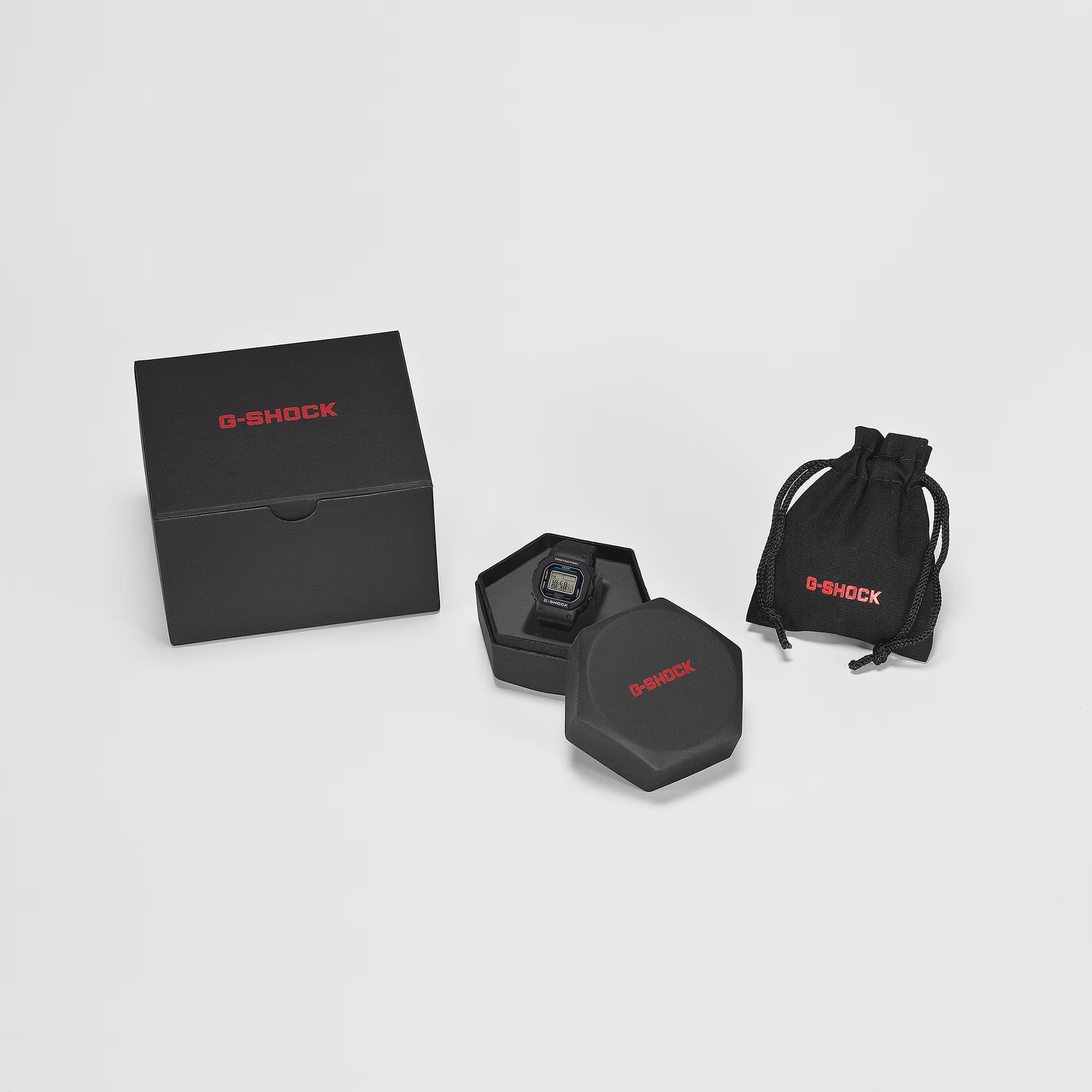 Casio G-SHOCK Nano DWN5600-4 miniature watch. 1/10-scale red version of the DW-5600 made from sustainable bio-based resin. Features 23.4 × 20 × 7.5 mm case, 6 g weight, LED backlight with time flash, dual time, stopwatch, and auto-calendar. Shock resistant and 200-meter water resistant. Includes special silicone display stand and approx. 2-year SR621SW battery