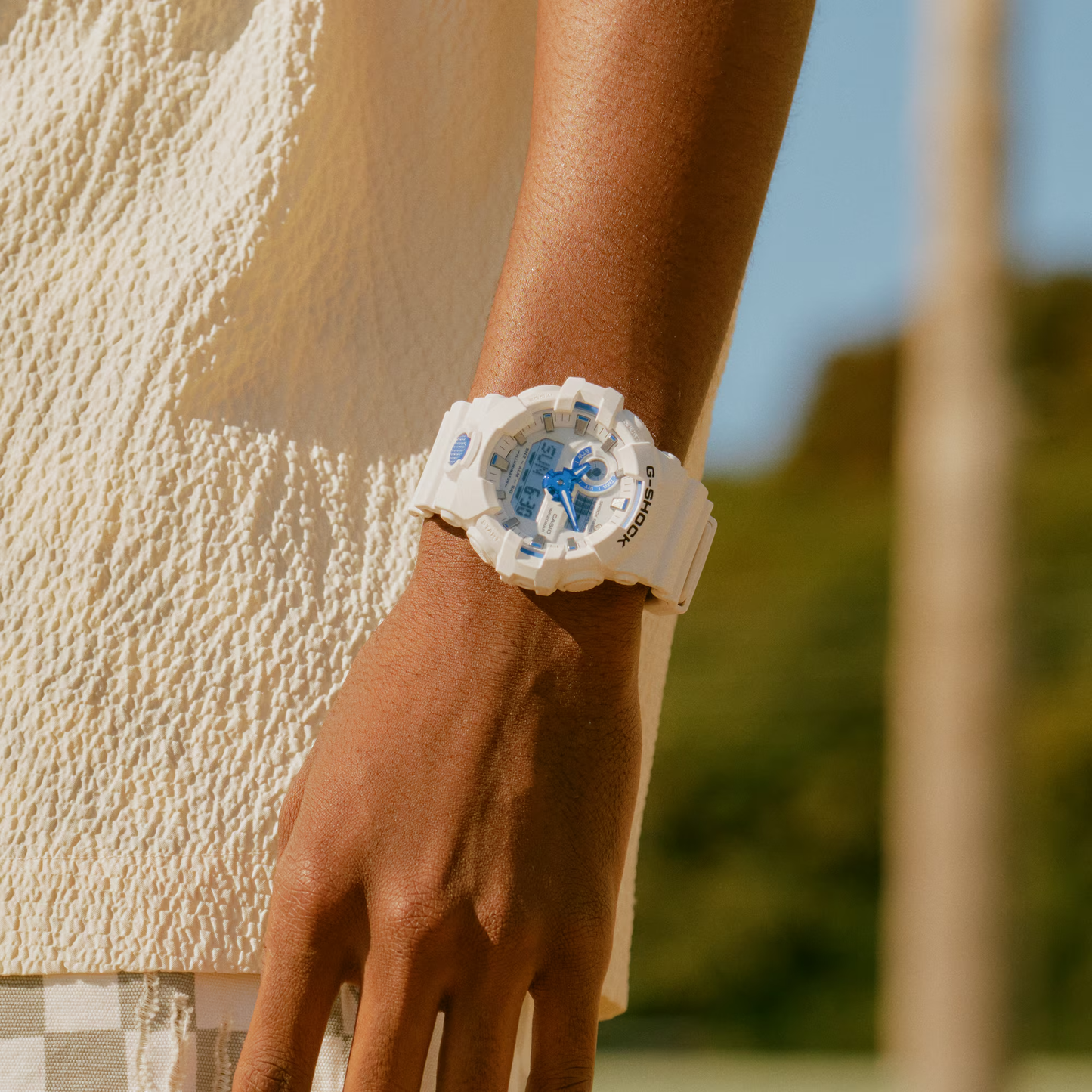 Person wearing a white watch with blue floral design on a blurred natural background