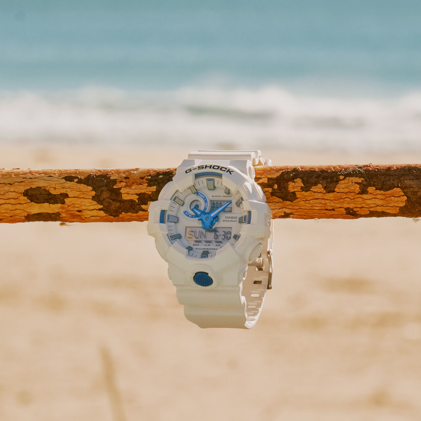 White Casio G-Shock watch with blue accents on a wooden surface with a beach background