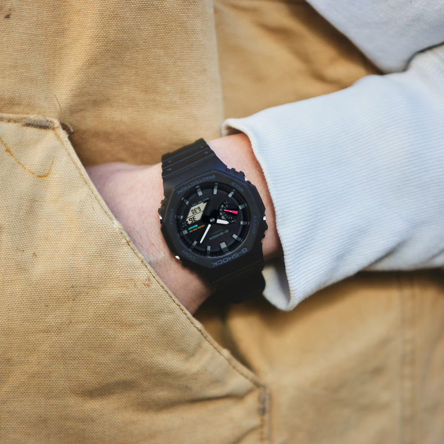 Black wristwatch on a person's wrist with a beige jacket background