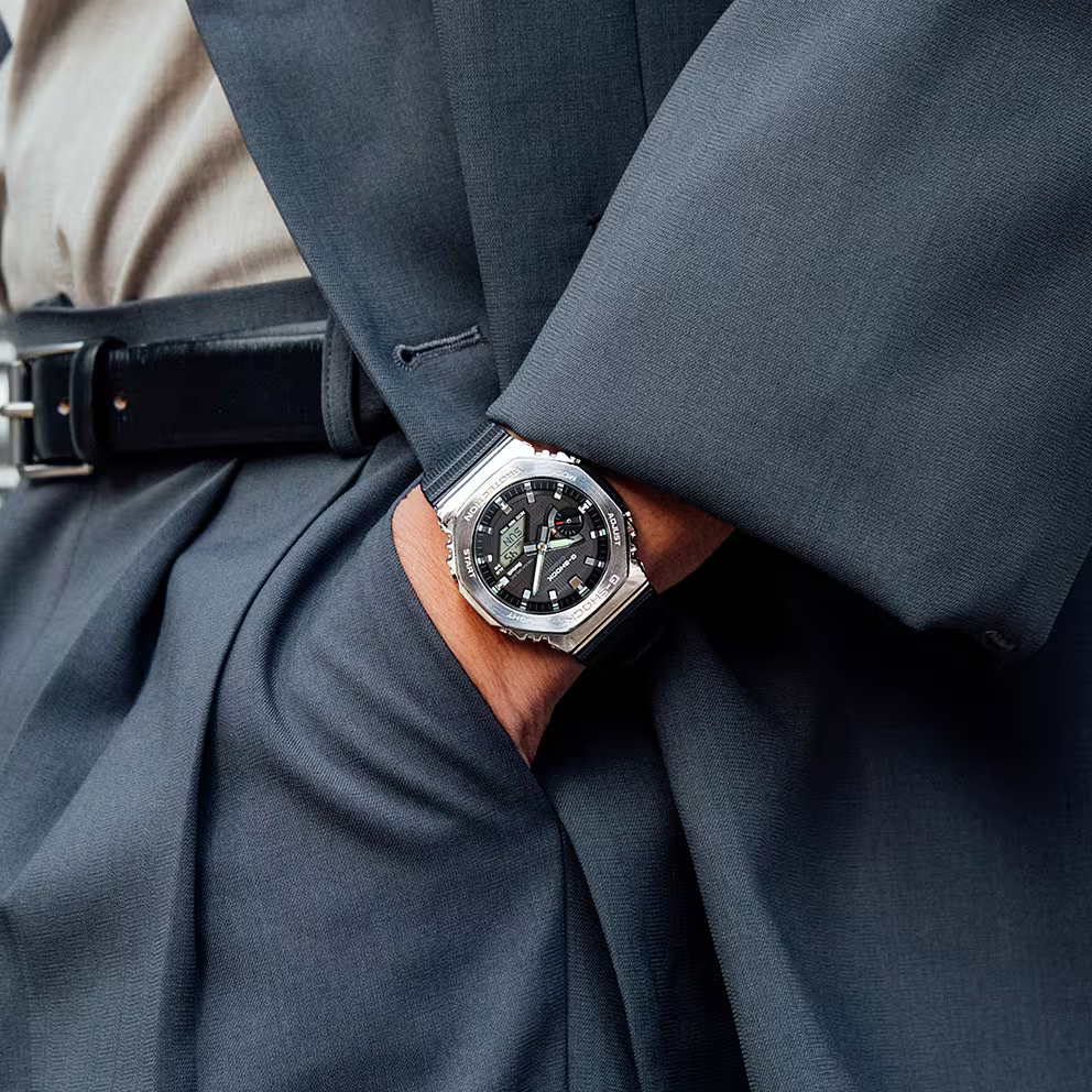 Close-up of a person wearing a dark gray suit with a brown leather watch on a neutral background