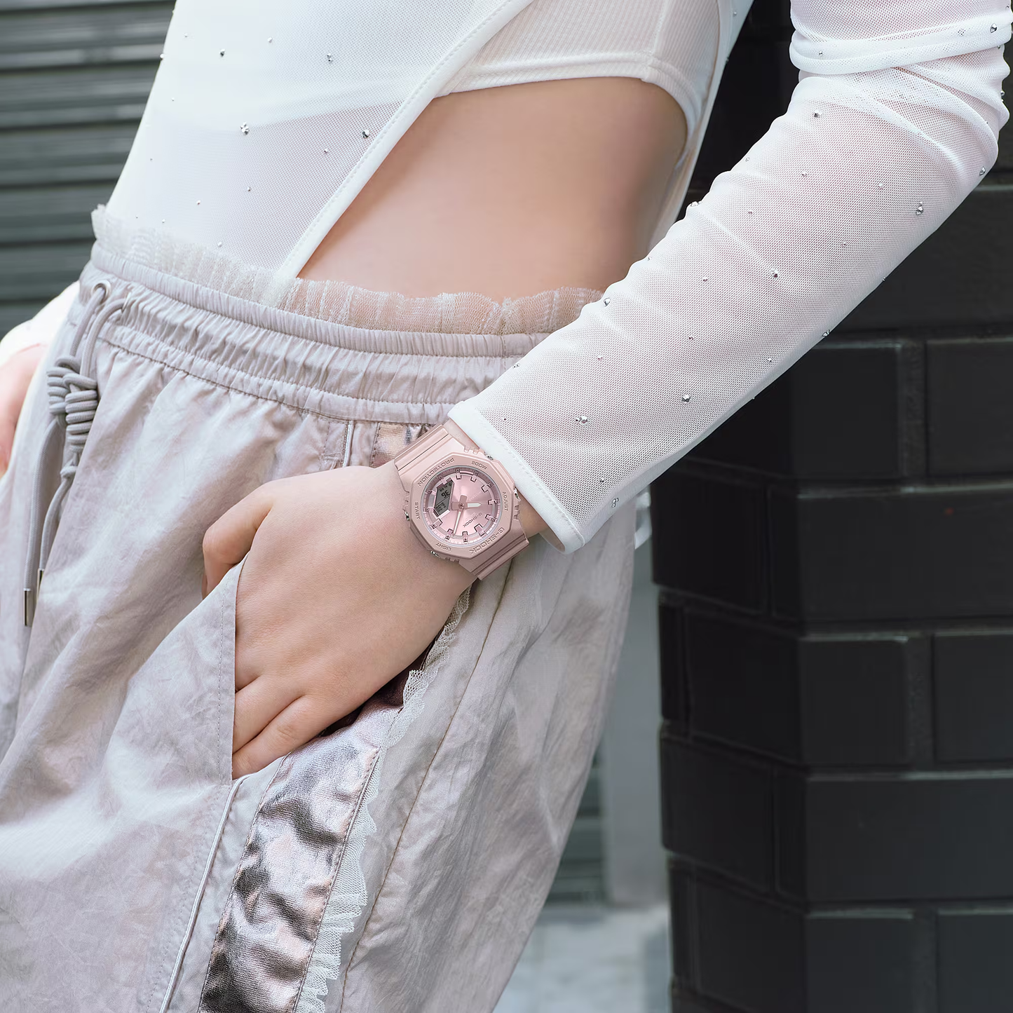 Person wearing a pink smartwatch with a white long-sleeve shirt and beige pants.