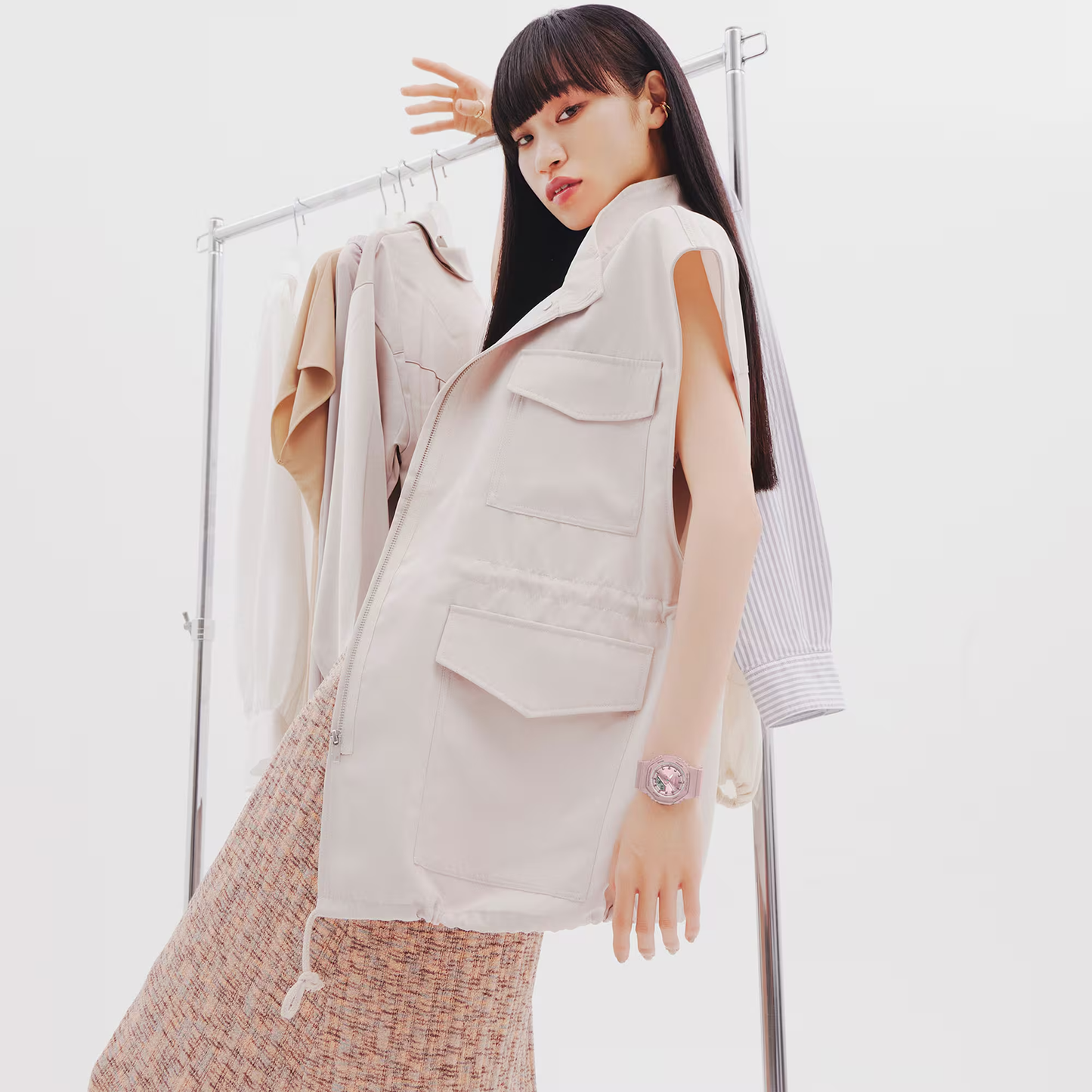 Woman wearing a beige vest and patterned pants standing in front of a rack with clothes.