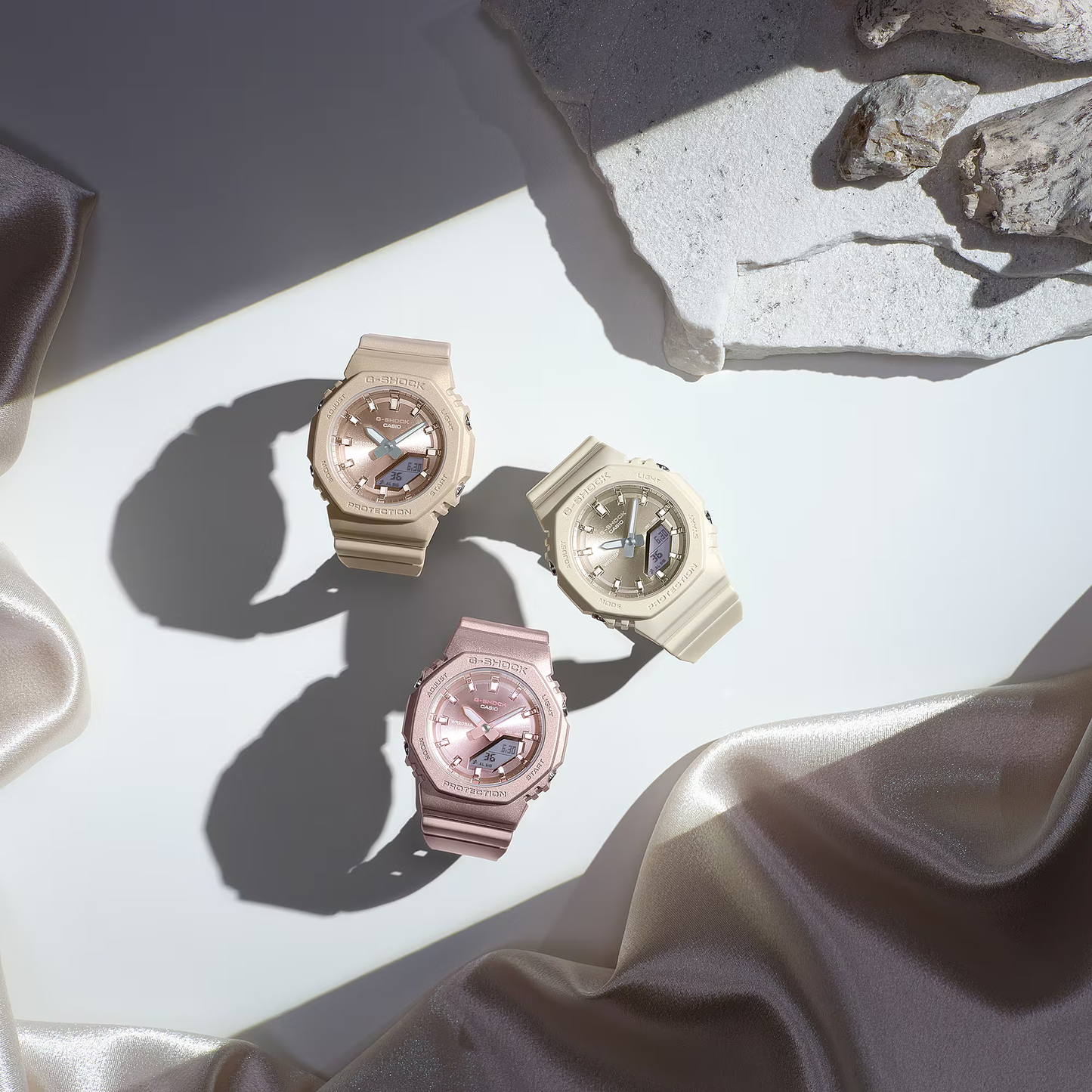 Three watches in rose gold on a light fabric surface with stone background