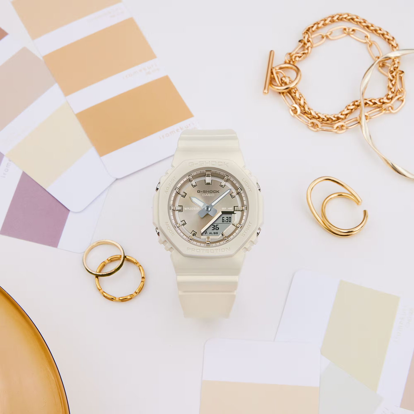 Beige Casio watch with gold jewelry on a color swatch background
