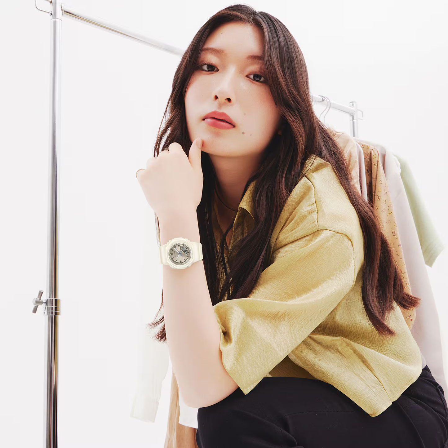 Woman wearing a yellow shirt and a watch, standing in a minimalistic setting.