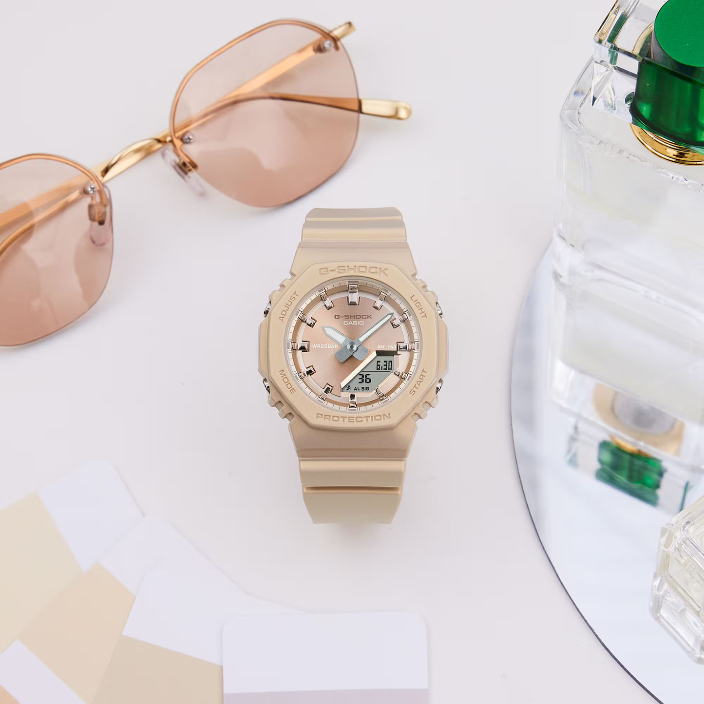 Beige Casio watch with sunglasses and perfume bottle on a white surface