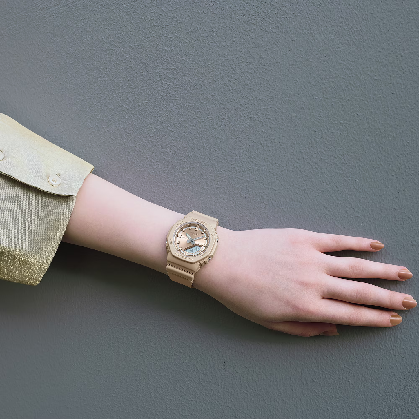 Gold wristwatch on a person's wrist against a gray background