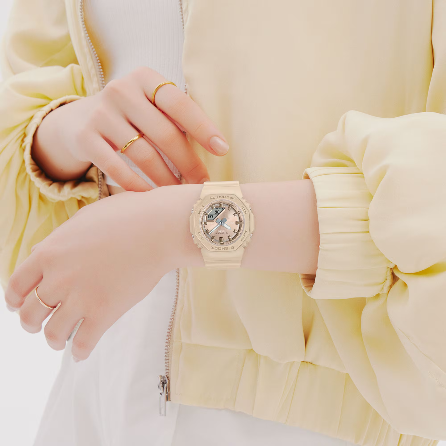 Person wearing a gold watch on a light yellow jacket