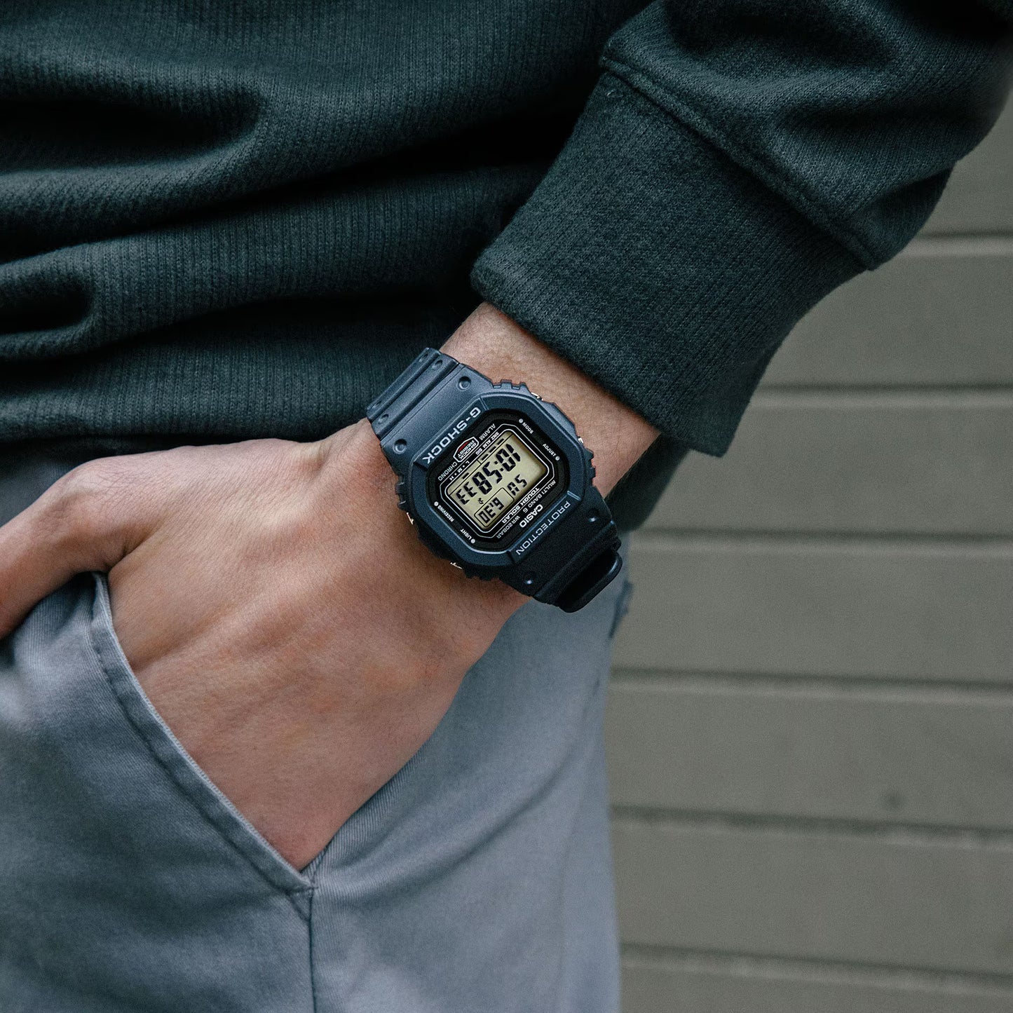 Person wearing a black digital watch on a neutral background