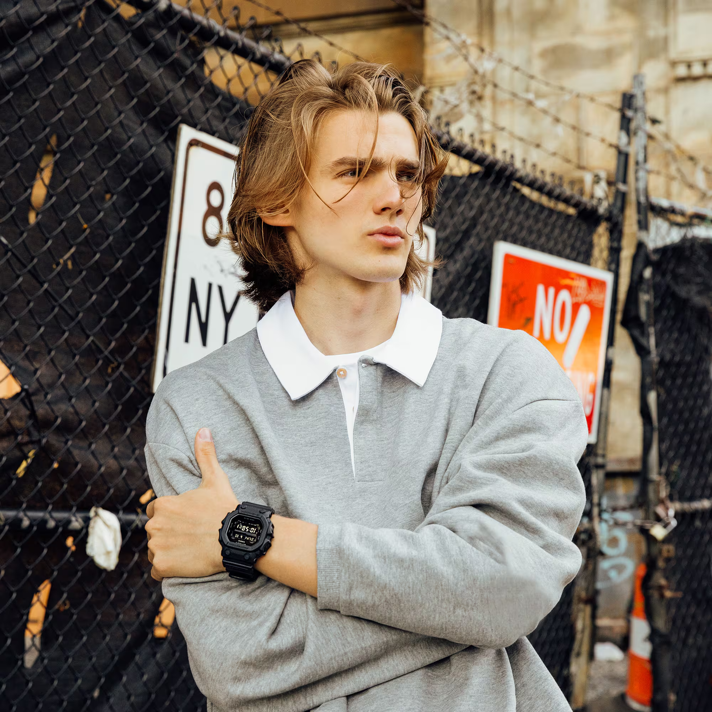 Man in gray sweater with white collar giving a thumbs-up in an urban setting