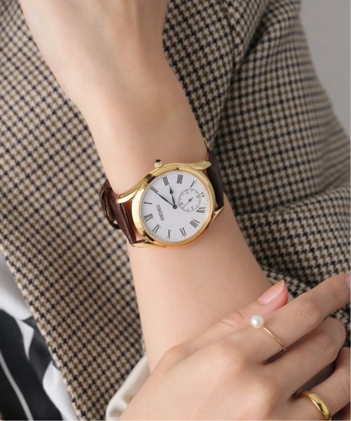 Seiko SRK050 – classic gold-tone dress watch with white Roman numeral dial, seconds subdial, cabochon crown, and brown leather strap; refined elegance from the Essentials Collection.