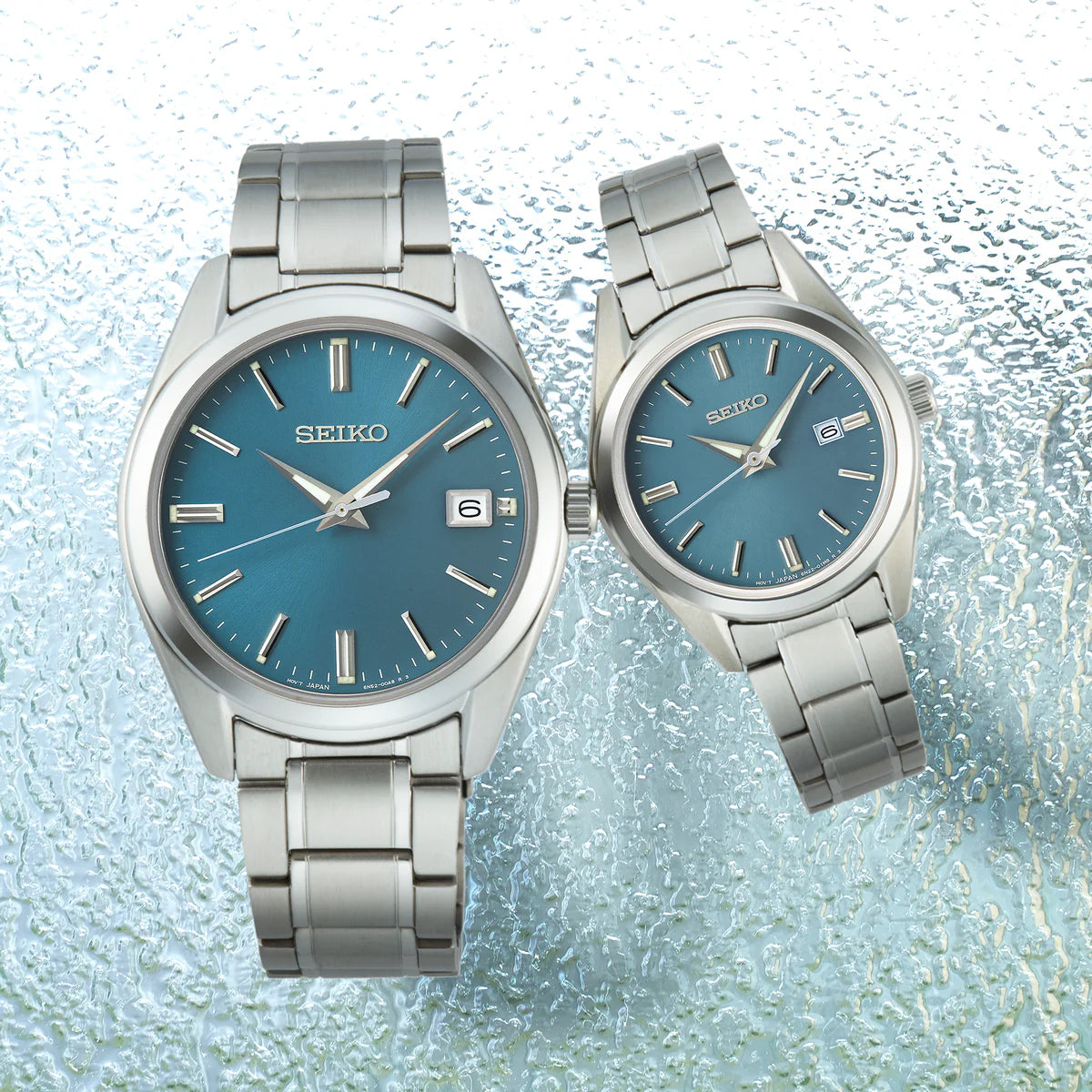 Two Seiko watches with blue faces and silver metal bands on a textured light blue background.