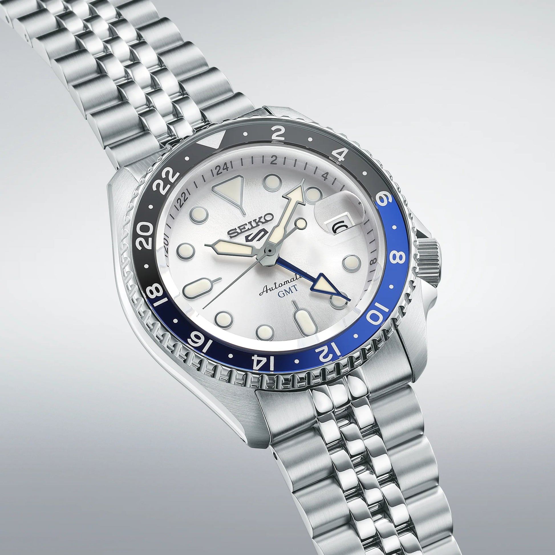 Seiko SSK033 GMT automatic watch with silver sunray dial, dual-tone blue and black 24-hour bezel, luminous hands, magnified date display, and stainless steel five-row bracelet — SKX-inspired GMT model available at Miseki Jewelry