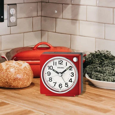 SEIKO QHE196RLH red bedside alarm clock displayed on a kitchen counter, featuring compact square design and easy-to-read analog dial.