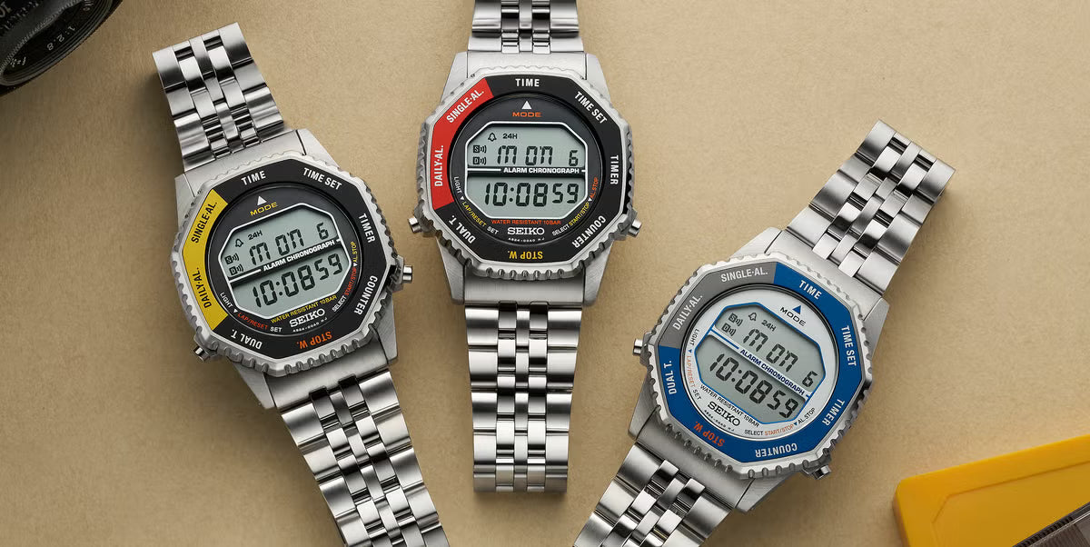 Three digital watches with metallic straps on a beige background