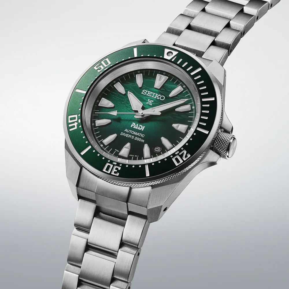 Seiko watch with green dial and silver metal bracelet on a light gray background