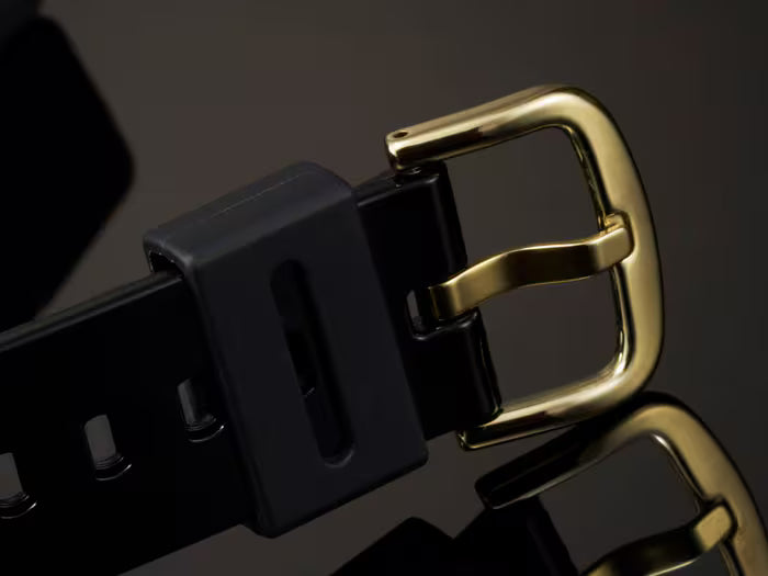 Black and gold belt buckle on a reflective surface with a dark background
