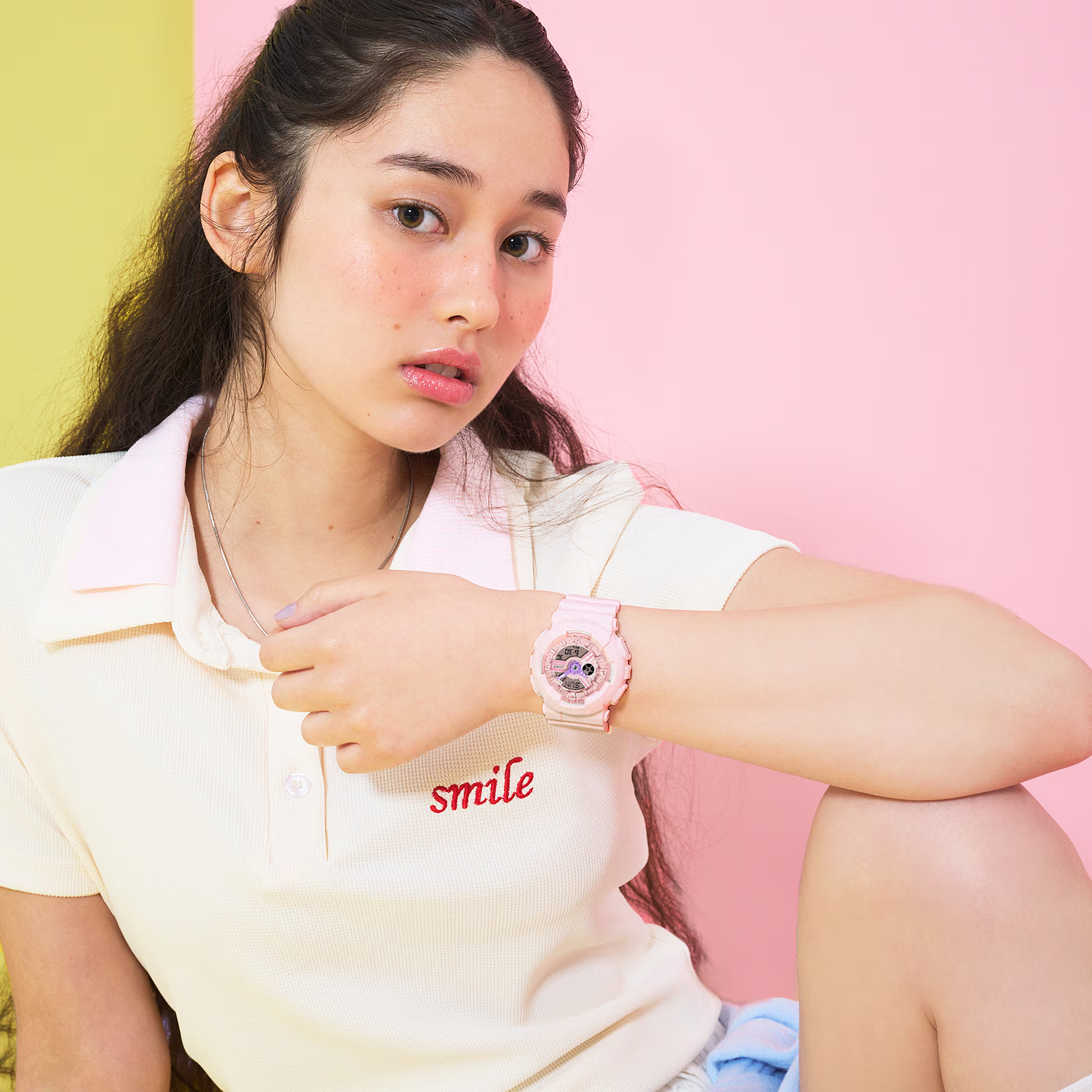 Woman wearing a white shirt with 'smile' text and a pink watch against a pink background