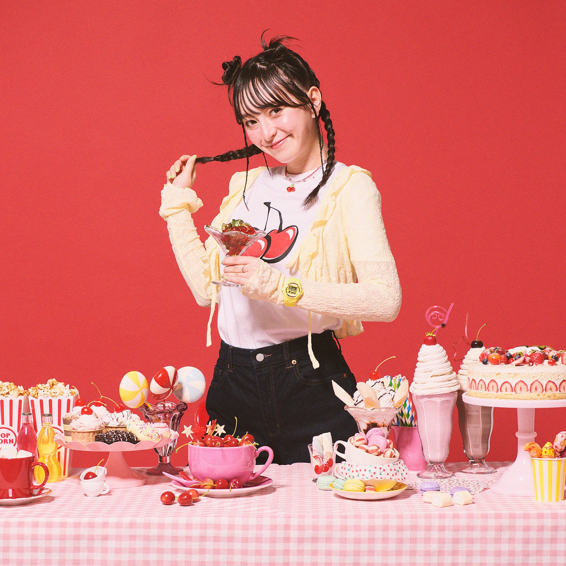 Person with braided hair in a room with a red background and various desserts on a table.