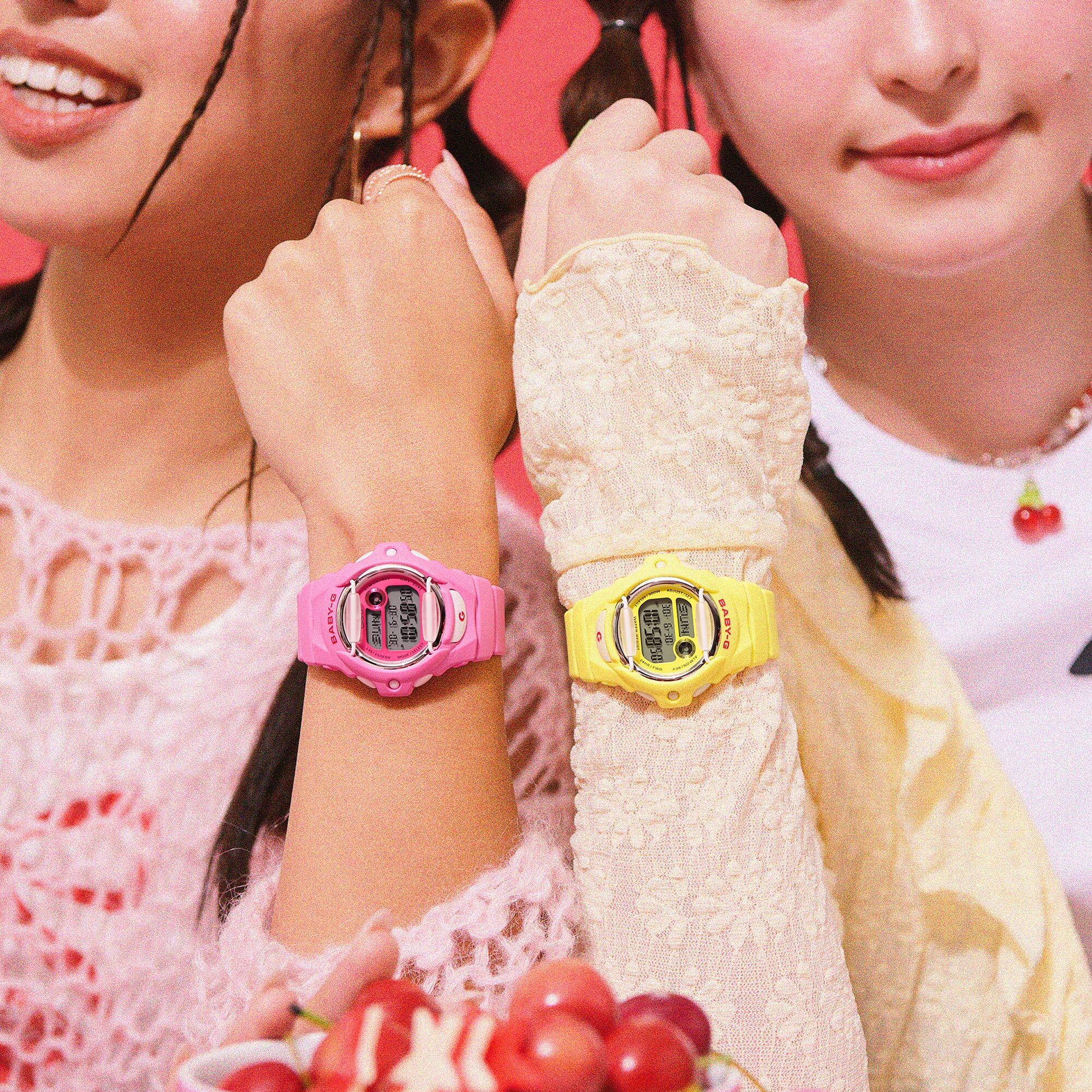 Two girls wearing colorful digital wristwatches, one pink and one yellow, with a close-up focus on their wrists.