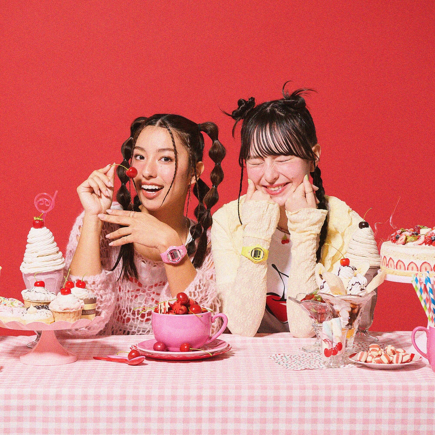 Two women sitting at a table with desserts and drinks against a red background