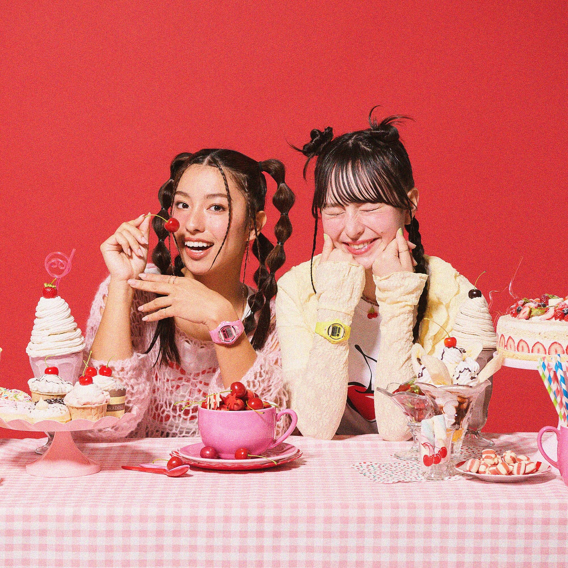 Two women sitting at a table with desserts and drinks against a red background