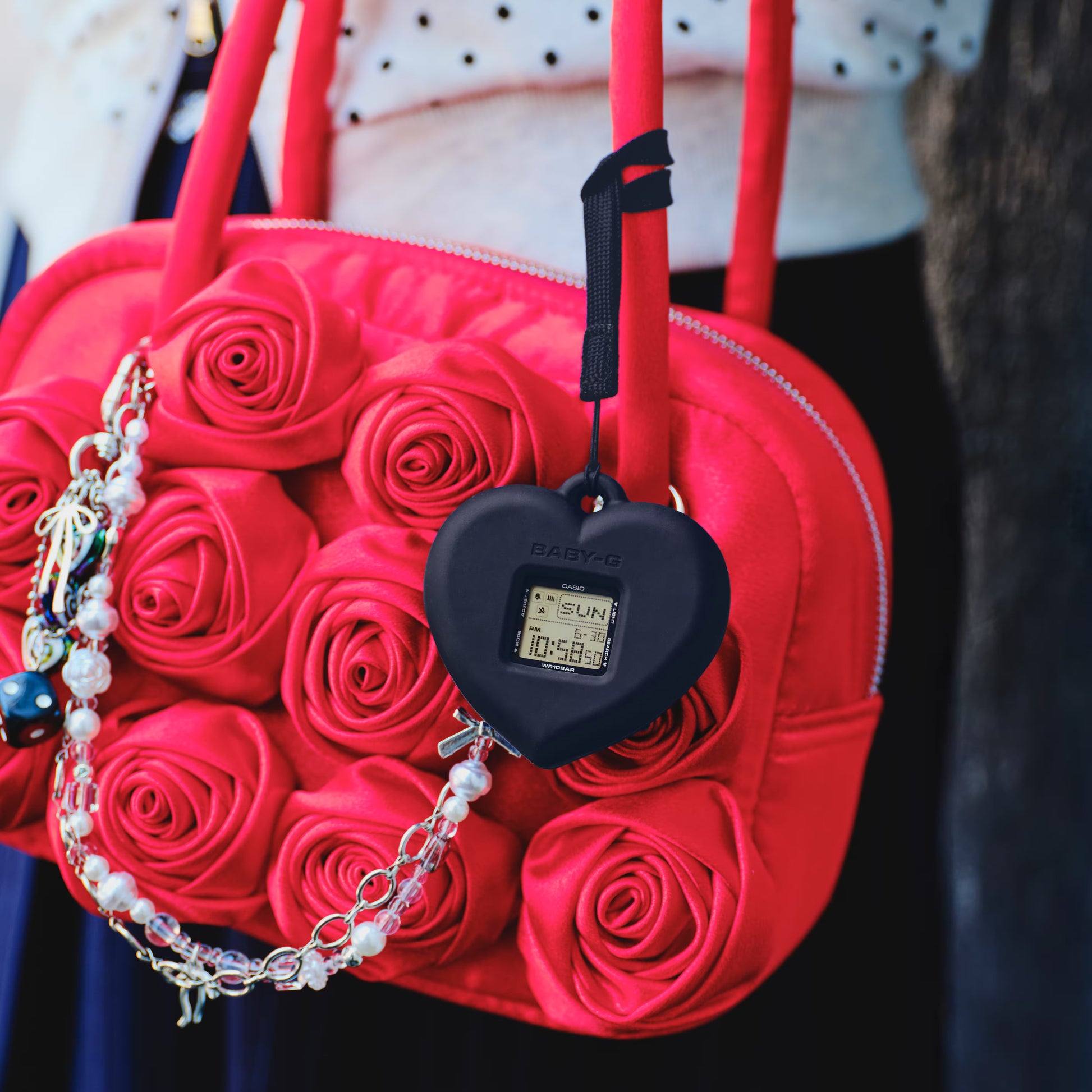 Red rose-patterned handbag with a heart-shaped digital device attached, on a blurred background.
