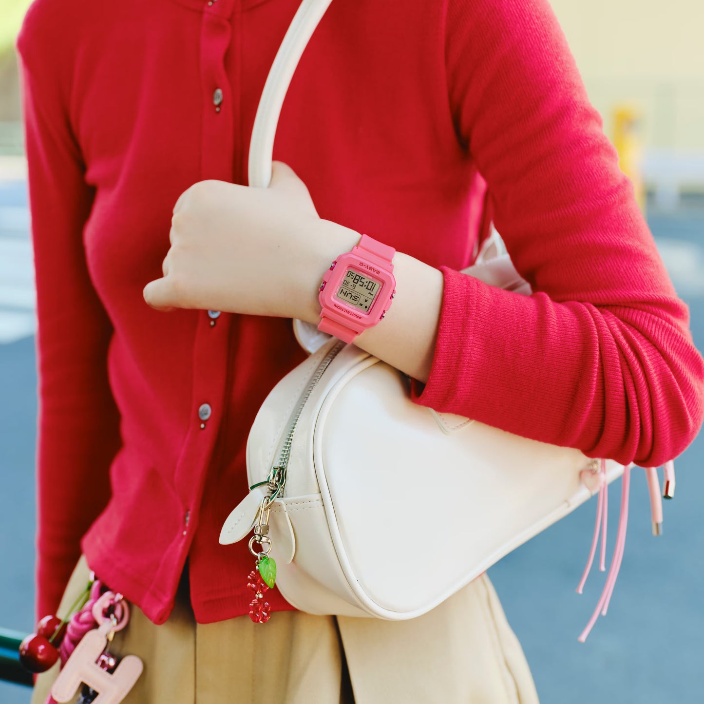 Person wearing a pink digital watch with a white bag and red cardigan.