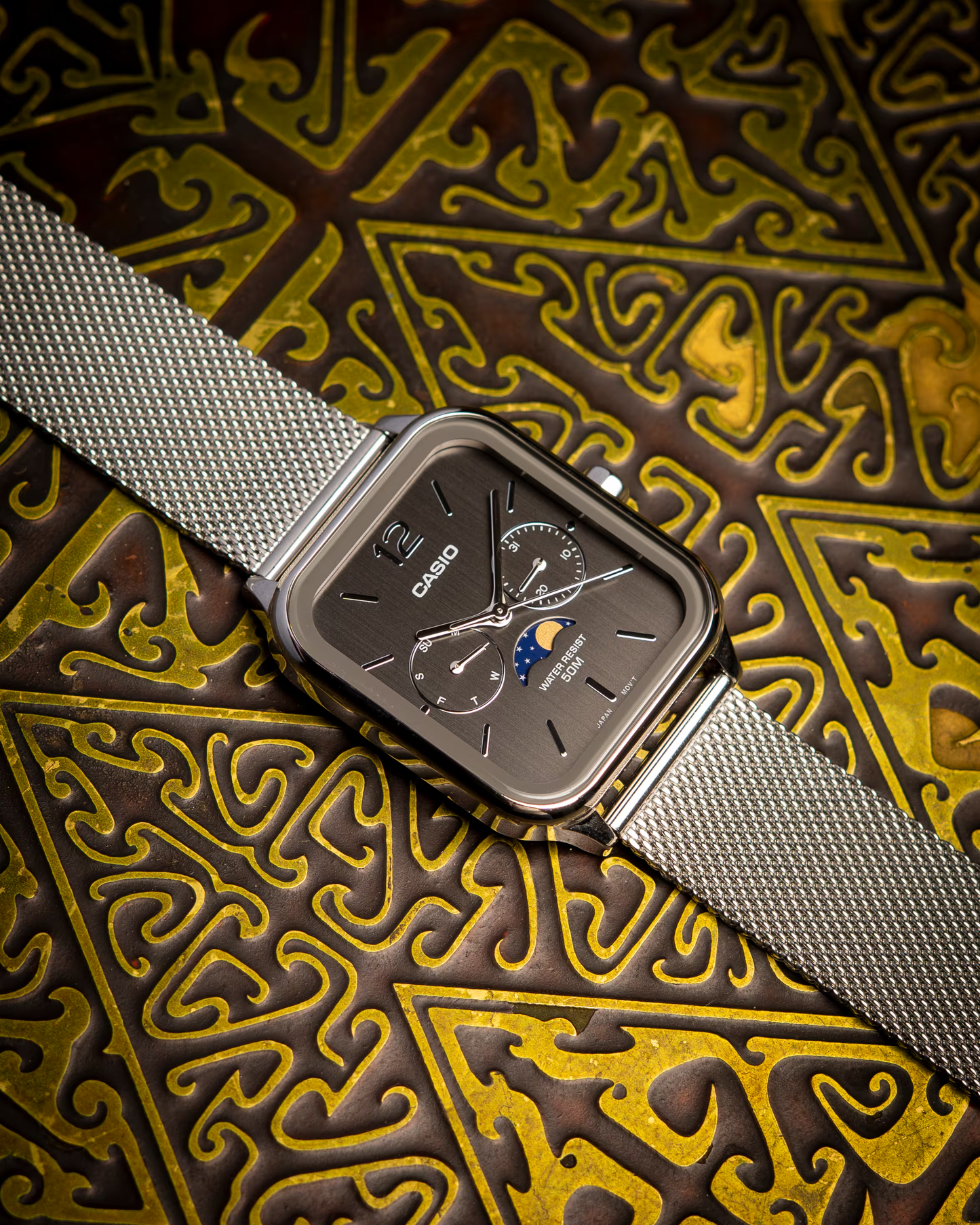 Casio watch with silver mesh strap on an ornate gold and brown background