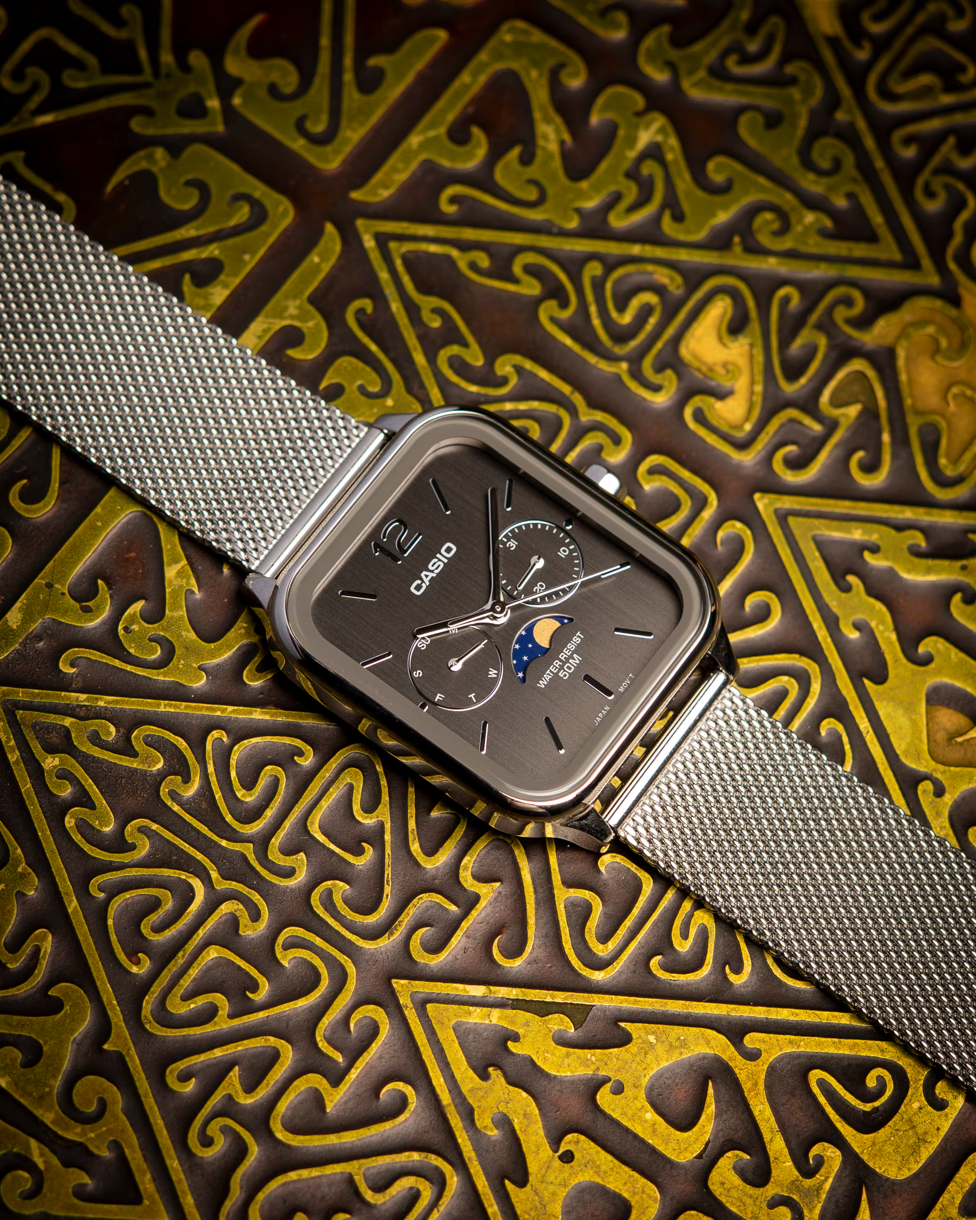 Casio watch with silver mesh strap on an ornate gold and brown background