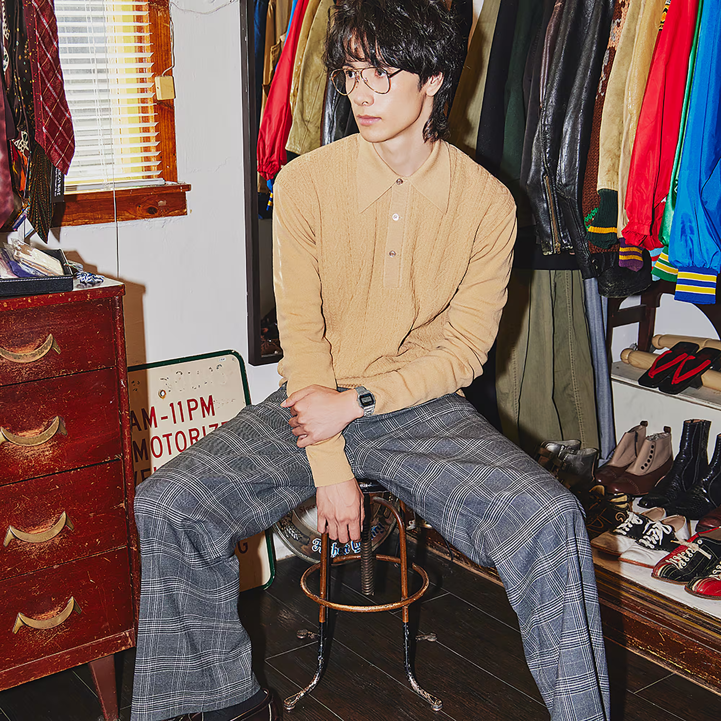 Person sitting on a stool in a room with vintage clothing and shoes around