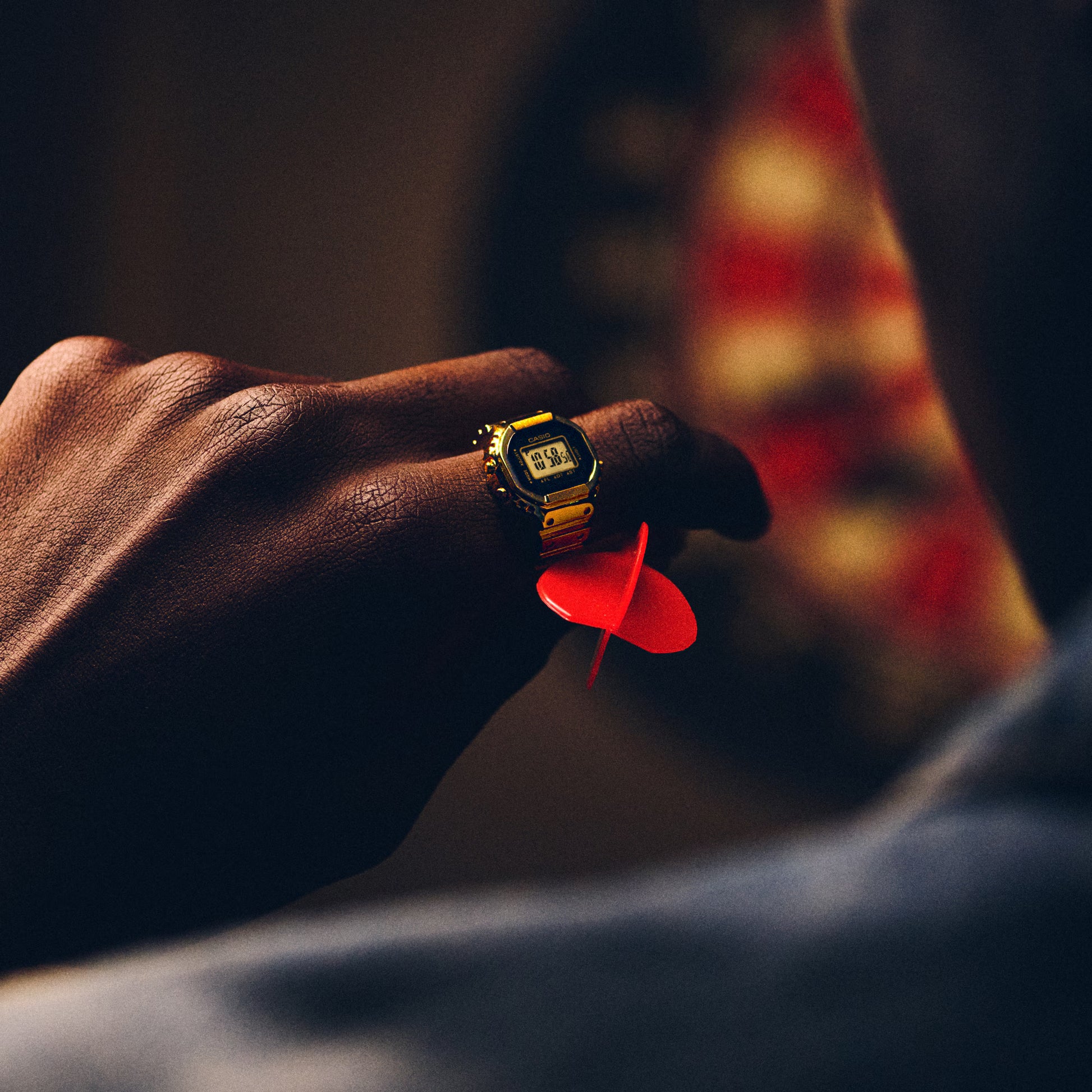 Hand holding a red dart with a digital watch on a blurred background