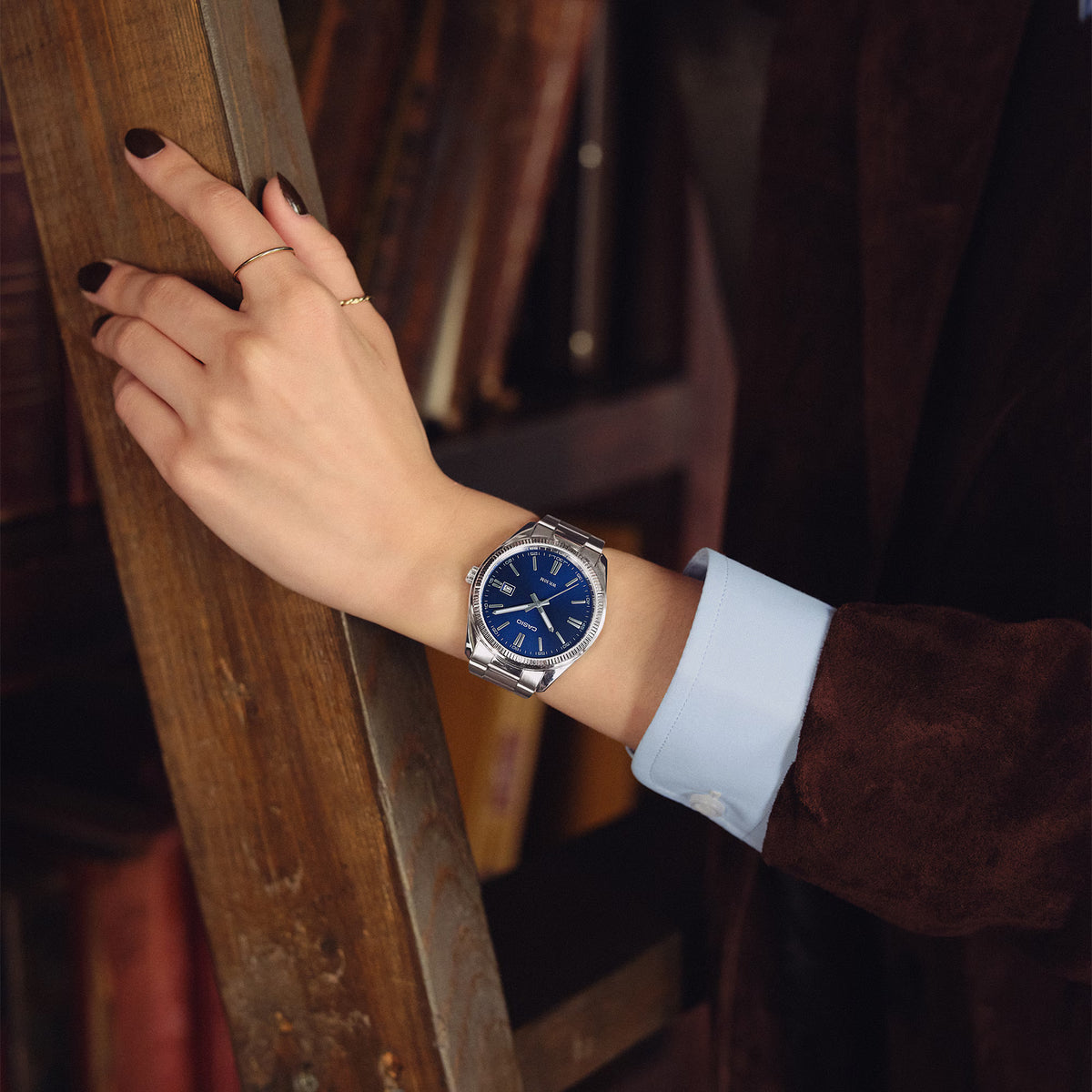 CASIO MTP1302D-2AVT blue dial stainless steel watch worn on the wrist in a classic library-style setting.