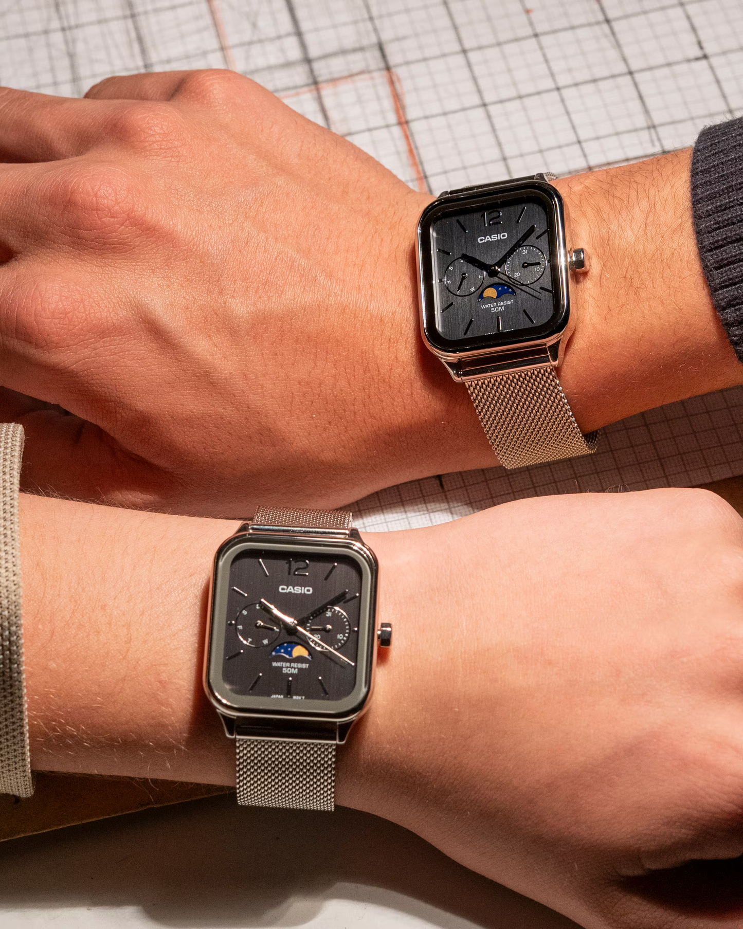 “Casio Standard MTPM305MC-1AV men’s analog watch with stainless steel rectangular case, black dial, moon phase display, date and day sub-dials, mineral glass, 50m water resistance, and stainless steel mesh band.