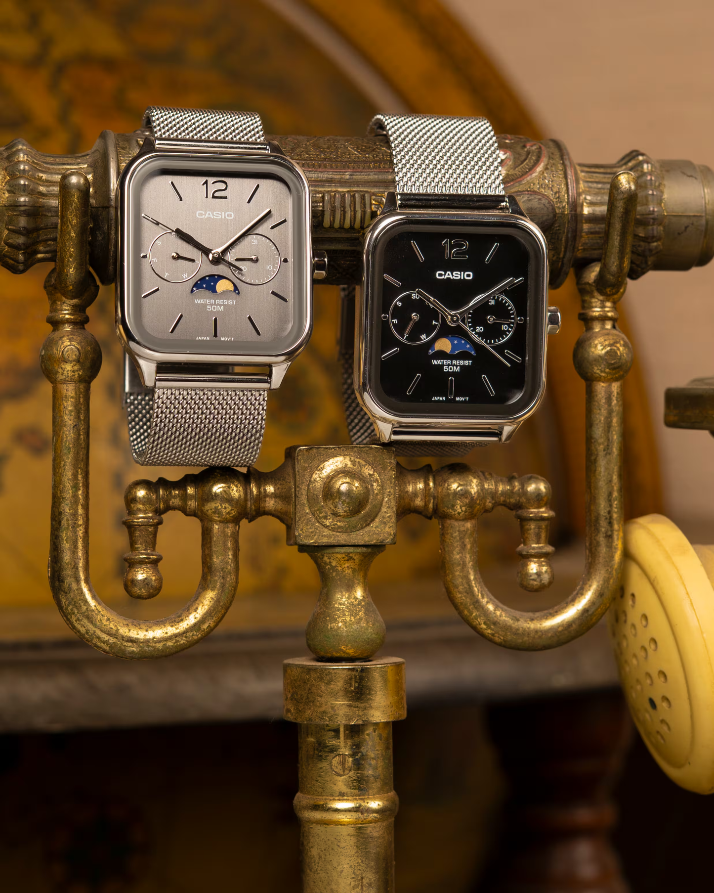 “Casio Standard MTPM305MC-1AV men’s analog watch with stainless steel rectangular case, black dial, moon phase display, date and day sub-dials, mineral glass, 50m water resistance, and stainless steel mesh band.