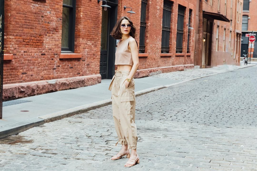 Woman in beige outfit standing on a street with brick buildings.