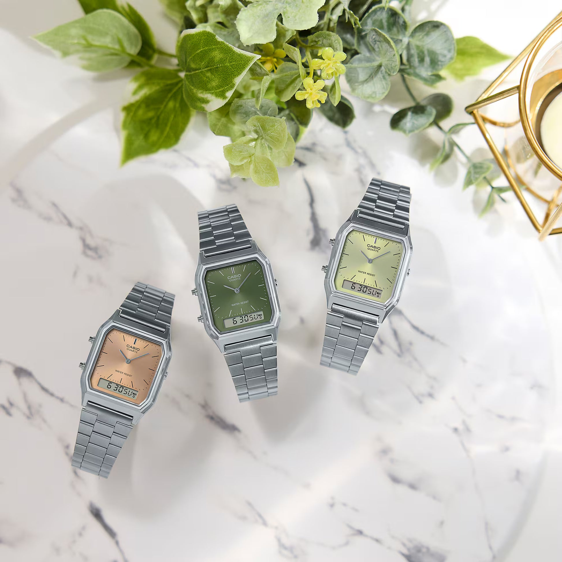 Three vintage-style watches on a marble surface with greenery in the background